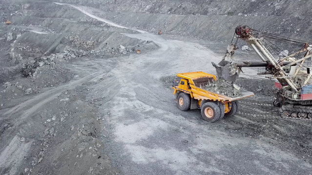 Top view of excavator in open pit. Excavator falls asleep rubble in dumper on outdoor quarry in extraction of minerals. Concept of extraction of minerals