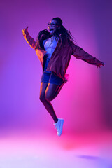 Studio shot of young excited woman in casual style outfit jumping isolated on purple background. Concept of beauty, art, fashion, youth, style