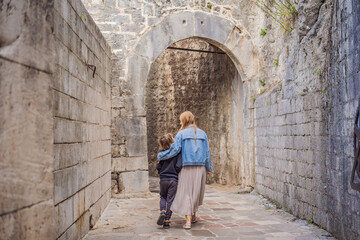 Fototapeta na wymiar Mom and son travelers enjoying Colorful street in Old town of Kotor on a sunny day, Montenegro. Travel to Montenegro concept