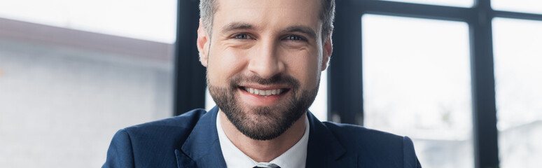 Obraz premium cheerful bearded businessman smiling at camera in office, banner.