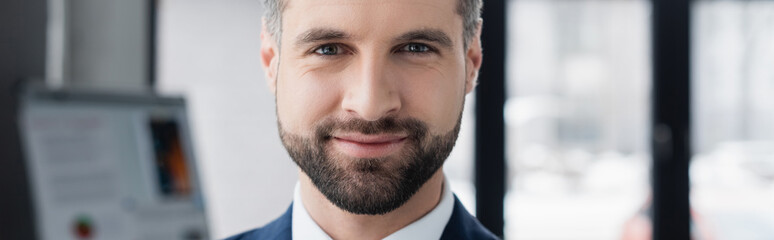 Fototapeta premium portrait of happy bearded economist smiling at camera in blurred office, banner.