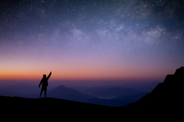 Naklejka premium Silhouette of young traveler and backpacker standing and open arms watched the star and milky way alone on top of the mountain. He enjoyed traveling and was successful when he reached the summit.