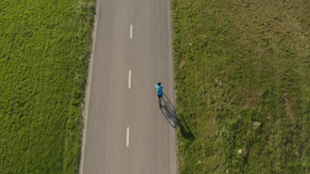 Racing cyclist riding on an empty flat asphalt road, aerial top down drone shot.