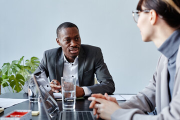 Portrait of young African American executive talking to female colleague during business meeting in office against pale blue wall