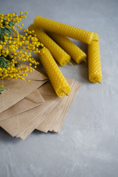 Candles made of natural honey wax. Craft envelopes for letters. A branch of yellow mimosa. Vertical image.