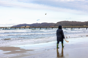 A woman in a winter jacket and boots walks along the seashore.