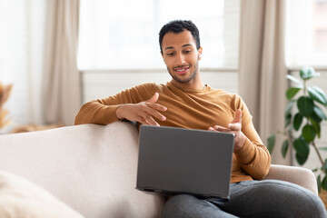 Arab man using laptop wearing headphones sitting on couch