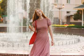 Young beautiful red-haired long-haired woman in a summer pink dress walks through the streets of a summer city.