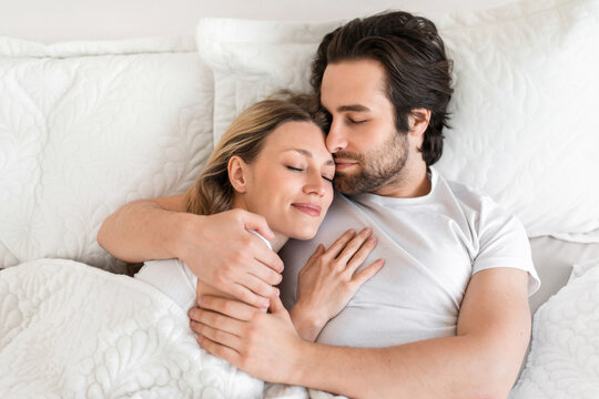 Top view of young affectionate couple sleeping in bed, embracing each other. Loving relationships and marriages