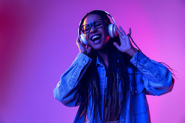 Music. Beautiful girl in headphones listening to music isolated on purple background in neon light. Concept of beauty, art, fashion, youth and emotions