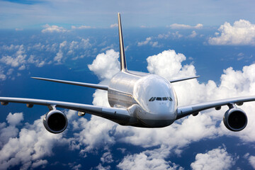 The passenger widebody plane in flight. Aircraft flies high in the blue sky above clouds. Airplane closeup front view.