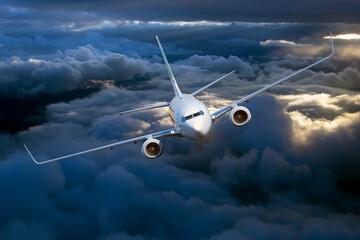 Passenger plane in flight. Aircraft flies high in the blue sky above the clouds. Front view. Left...