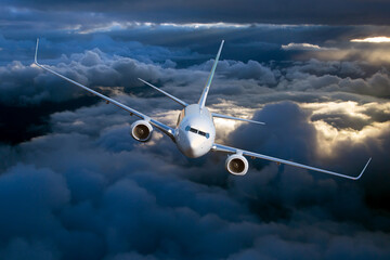 Passenger plane in flight. Aircraft flies high in the blue sky above the clouds. Front view. Right...
