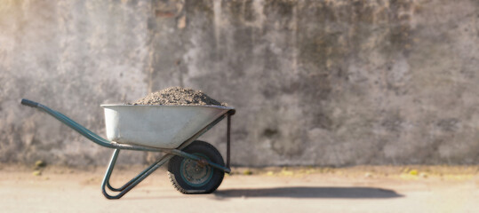 construction wheelbarrow with a pile of sand. a dirty construction wheelbarrow stands against a...