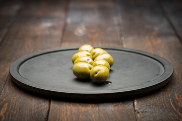 Big green olives on black plate on wooden table