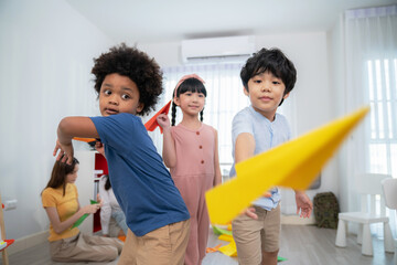 Asia and African kid playing paper rocket in the kindergarten school classroom. Rocket fly in front of camera.  Learning, enjoy, education, playing concept. Feeling happing and smile during class