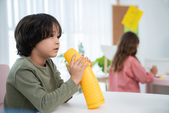 Handsome Boys Sitting In The Kindergarten School Classroom And Holding Cup Stacking Looking At Friend. Learning, Enjoy, Education, Playing Concept. Feeling Happing And Smile During Class