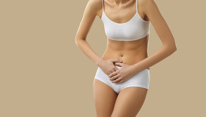 Fototapeta na wymiar Woman suffering from period cramps. Young lady in underwear standing isolated on beige background, feeling acute stomach ache or severe menstrual pain and holding hands on her belly, cropped shot