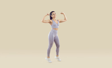 Fototapeta na wymiar Full length studio shot of happy cheerful smiling middle aged woman wearing lilac sports bra and leggings showing her fit, strong, attractive, healthy body. Regular fitness workout at gym concept