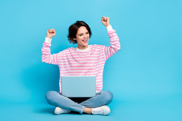 Photo of ecstatic pretty girl raise fists in victory achievement sit floor with laptop isolated on...