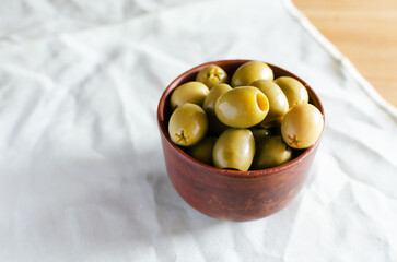 Pitted green olives in a ceramic bowl on a light napkin. The concept of vegetarian food. Russian style. Horizontal orientation. copy space.