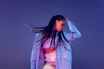 Emotional african girl in jeans and shirt dancing, having fun isolated on dark blue background....