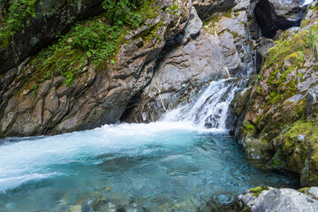Fresh water from a mountain stream flows over rocks into a blue shining natural water pool.