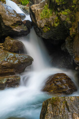 Naklejka na ściany i meble Between rocks falls a raging mountain stream of clear water photographed with motion blur.