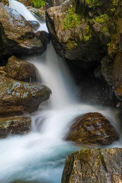 Between rocks falls a raging mountain stream of clear water photographed with motion blur.