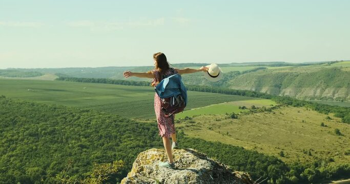 woman on the edge of a cliff, spreads her arms to the sides like a bird, The wind blows against the background of a green valley and a canyon