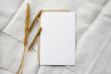 Stock stationery mock-up scene in a light key. Empty vertical greeting card and dried grains on white linen background.