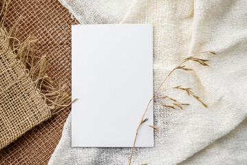 Stock stationery mock-up scene in a light key. Empty vertical greeting card and dried grains on white linen background.