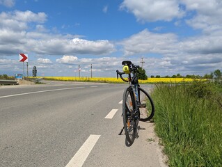 Fototapeta na wymiar A bike on a road during spring with a blue sky and a field of yellow flowers in the background.