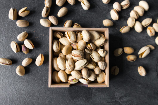 Pistachios in a small plate with scattered nuts of almonds around a plate on a vintage wooden table as a background. Pistachio is a healthy vegetarian protein nutritious food. Natural nuts snacks.