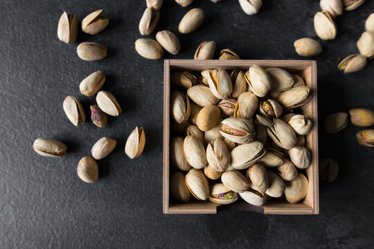 Pistachios in a small plate with scattered nuts of almonds around a plate on a vintage wooden table as a background. Pistachio is a healthy vegetarian protein nutritious food. Natural nuts snacks.