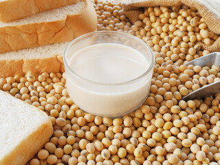 A cup of soy milk with a sack of soy bean and some breads for breakfast