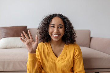 Positive young black woman waving at webcam, talking to family or friend on laptop from home