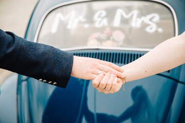 Bride and groom hold hands together. Retro wedding car