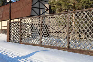 Beautiful bright house with a reddish-brown roof and a patterned carved fence. Winter.
