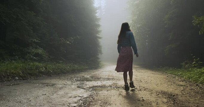 woman got lost in the forest. A lonely long-haired girl walks along a wet forest road into the fog. Look around you in a scary forest.