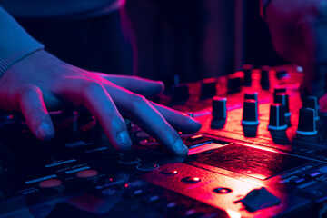 Close-up image in neon lights. Male hands turning sounds on professional dj mixer. Making sounds...