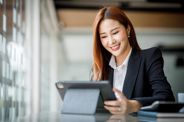 Portrait of Young Asian woman hand freelancer is working her job on computer tablet in modern office. Doing accounting analysis report real estate investment data, Financial and tax systems concept.