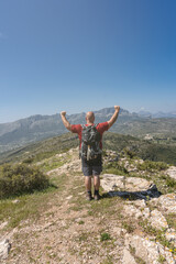 Fototapeta premium Unrecognizable man hiker with his arms raised, with a gesture of happiness and success, with mountains in the background