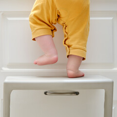 Toddler baby boy climbed with his feet on a high chair to climb on the kitchen cabinet. Child...