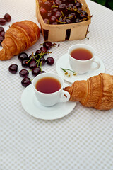Black tea with fresh croissants and cherries on the table against white background. Flat lay, spring breakfast conceptual composition