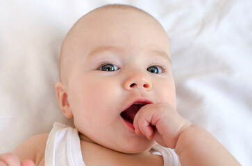 Baby sucks finger, fist. The baby grows the first tooth. Cute newborn in bed face close-up.