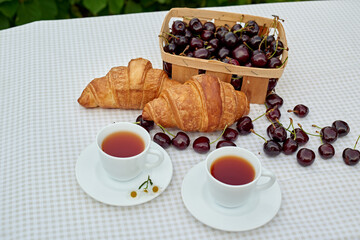 Black tea with fresh croissants and cherries on the table against white background. Flat lay, spring breakfast conceptual composition