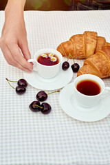 Black tea with fresh croissants and cherries on the table against white background. Flat lay, spring breakfast conceptual composition