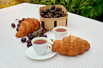 Black tea with fresh croissants and cherries on the table against white background. Flat lay, spring breakfast conceptual composition