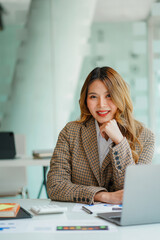 An Asian female accountant sits at a desk with a laptop and calculates financial graphs showing investment results. Plan a successful business growth process in the office.